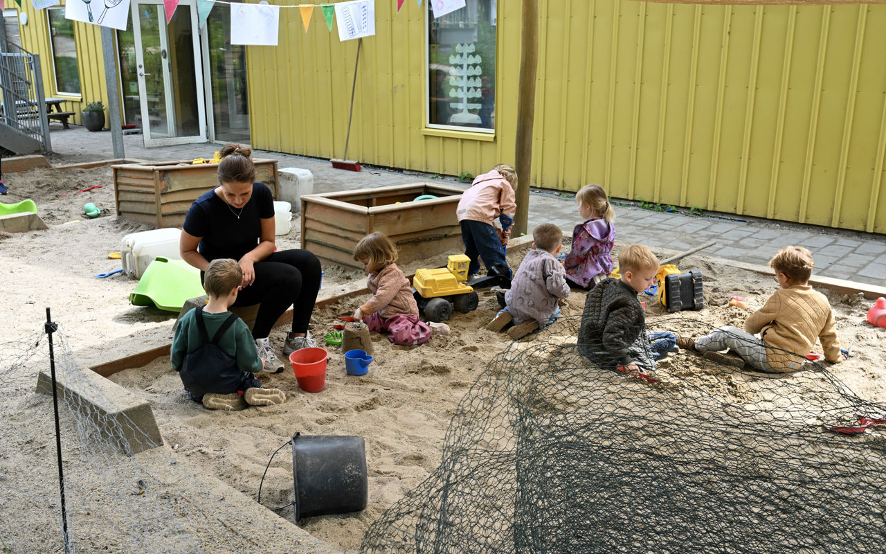 Voksen leger med børn i sandkasse
