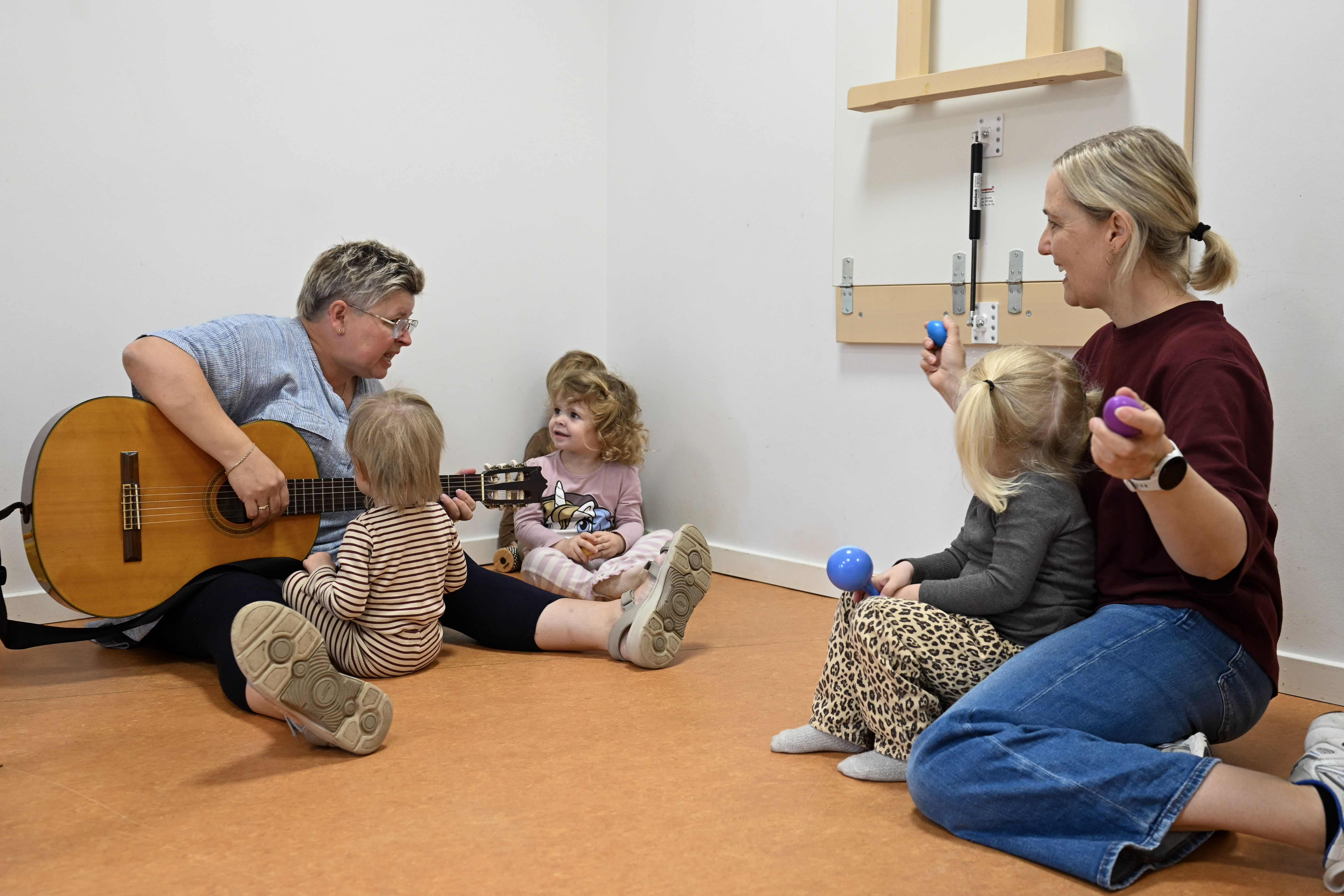 Voksen spiller guitar for børn, mens anden voksen og barn har rasleinstrumenter